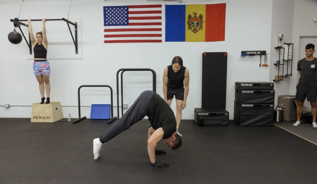 Clients working separate movements inside a Capra Bodyweight Training studio beneath American and Moldovan flags