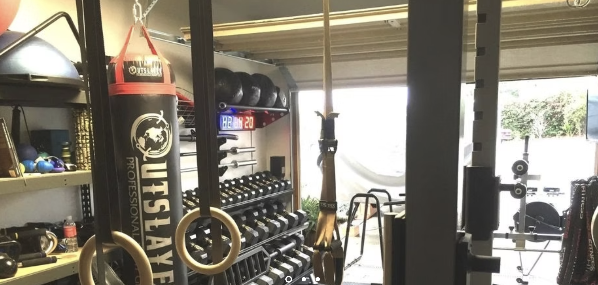 Close view inside Small Box Fitness showing gymnastic rings, a dumbbell rack, medicine balls, suspension straps, and an interval timer