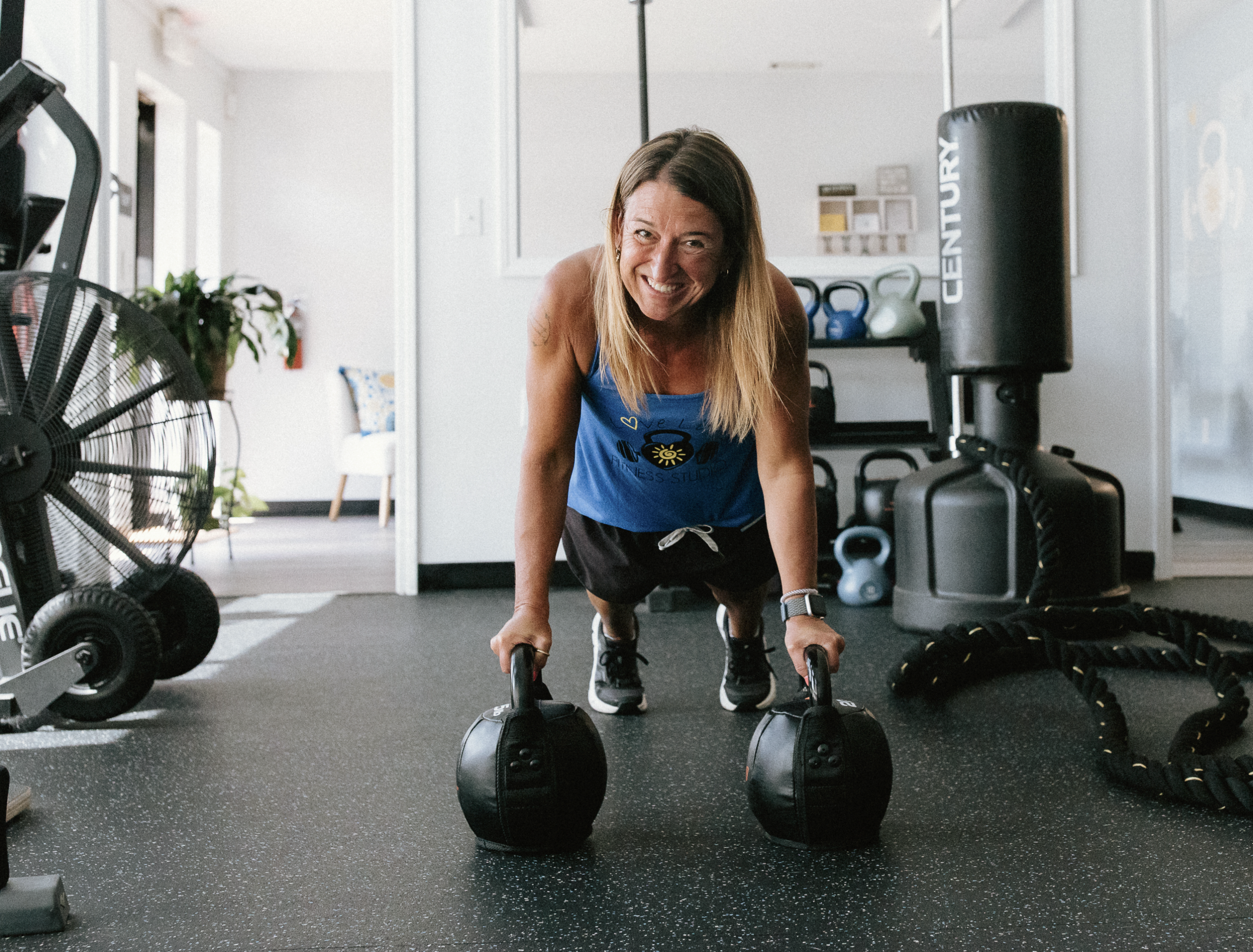 A woman smiling in a plank on two kettlebells on the Love Life Fitness studio floor in Fort Mill