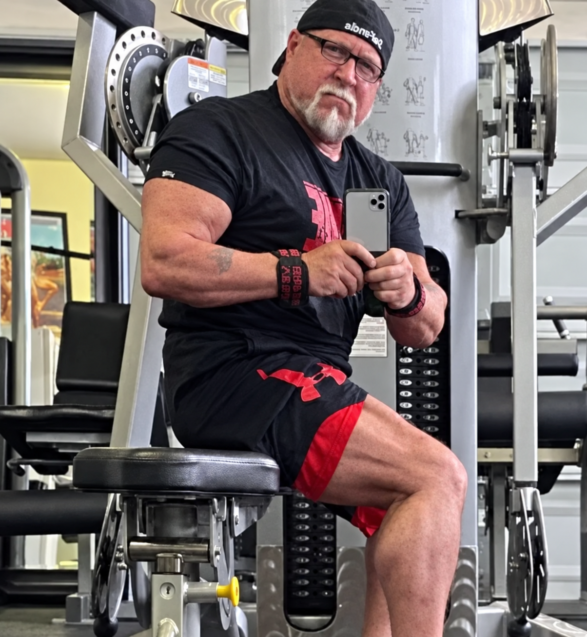 John DeFendis seated on a weight machine, taking a mirror photo in a gym lined with weight-stack equipment