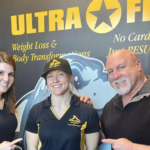 John DeFendis with two women in Ultra Fit shirts in front of an Ultra Fit wall graphic reading No Cardio: Just Results