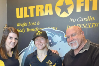 John DeFendis with two women in Ultra Fit shirts in front of an Ultra Fit wall graphic reading No Cardio: Just Results