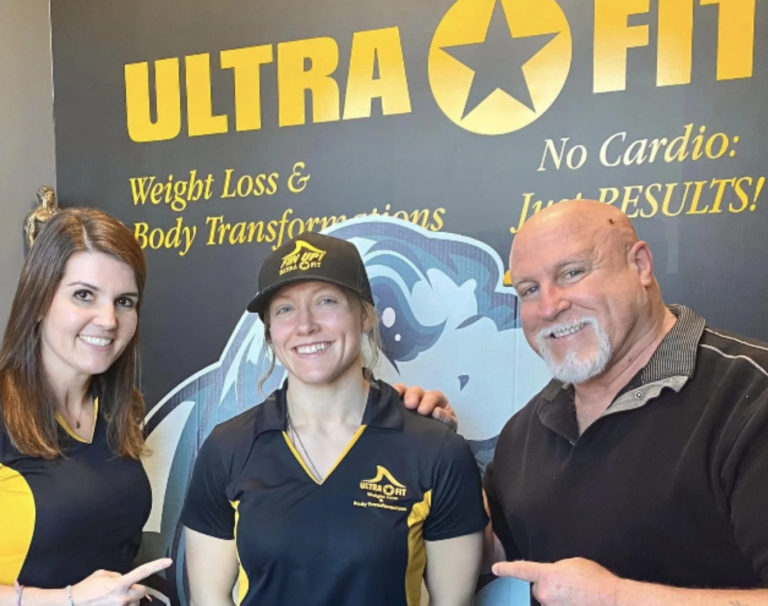 John DeFendis with two women in Ultra Fit shirts in front of an Ultra Fit wall graphic reading No Cardio: Just Results