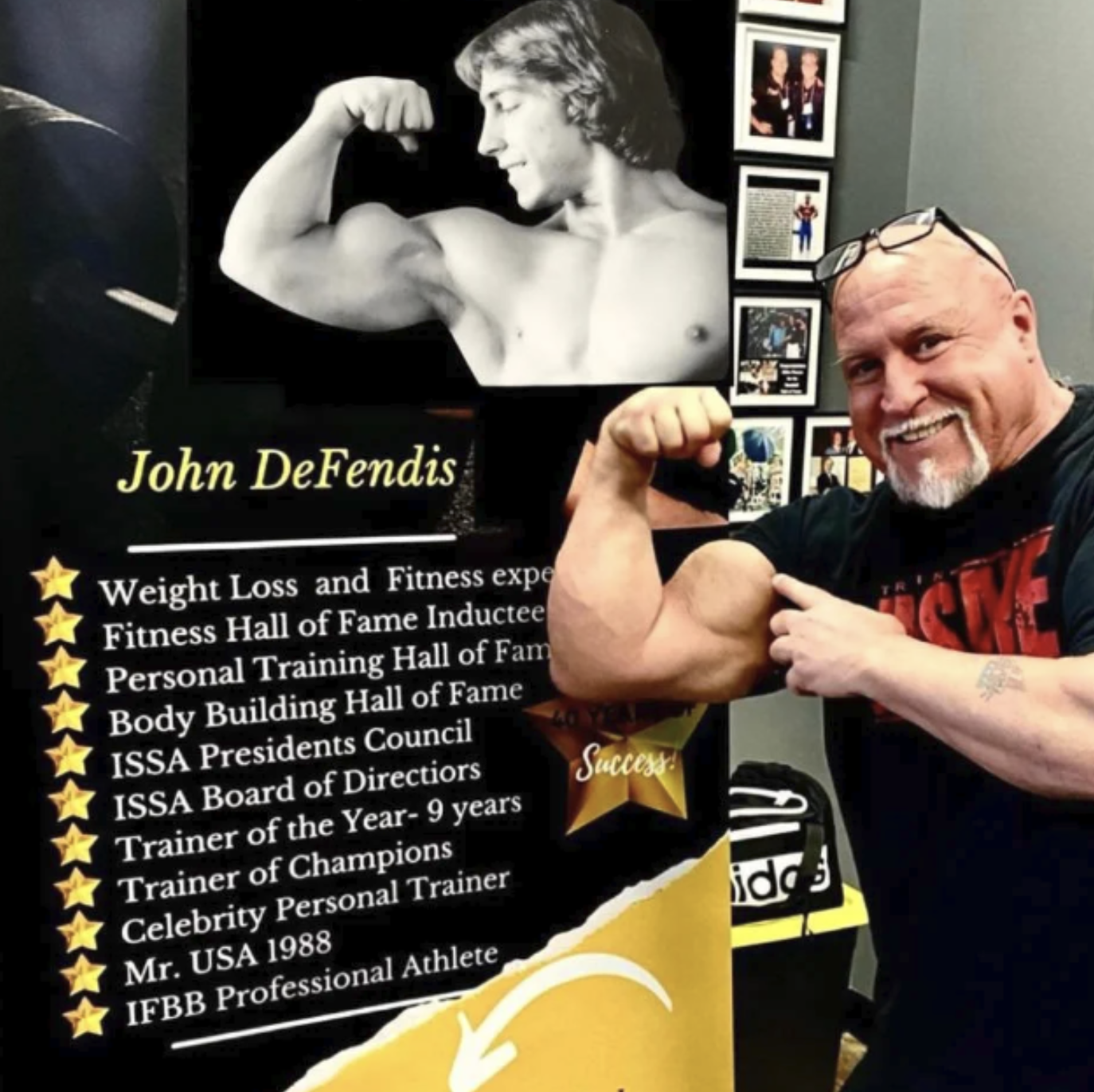 John DeFendis flexing his arm beside a display of an archival bodybuilding photo and a list of his credentials